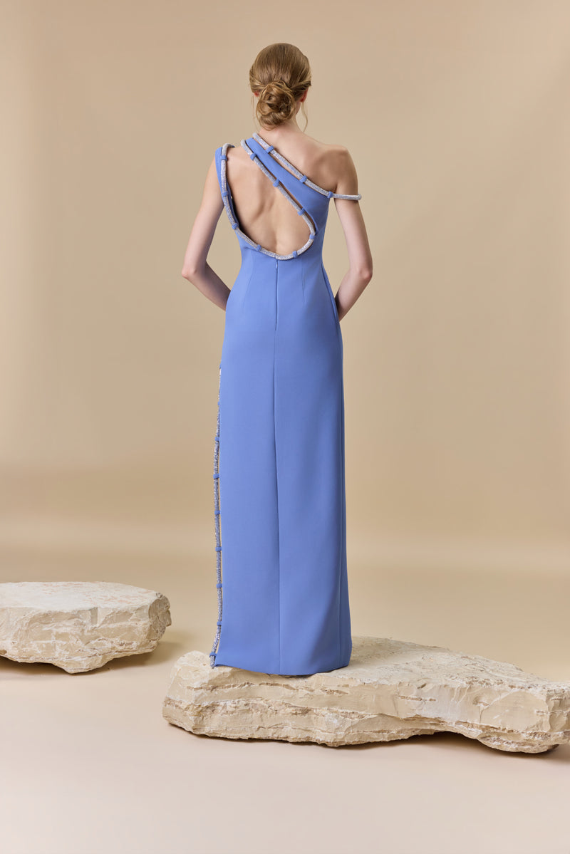 A fitted crepe gown featuring an asymmetrical neckline and a high side slit, both finished with crystal-embellished cord.