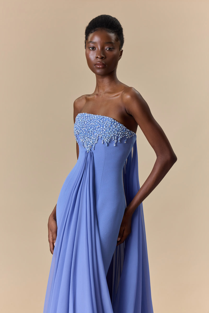 A strapless fitted crêpe dress featuring a straight neckline embellished with crystals with long, cascading chiffon drapes attached to the bodice.