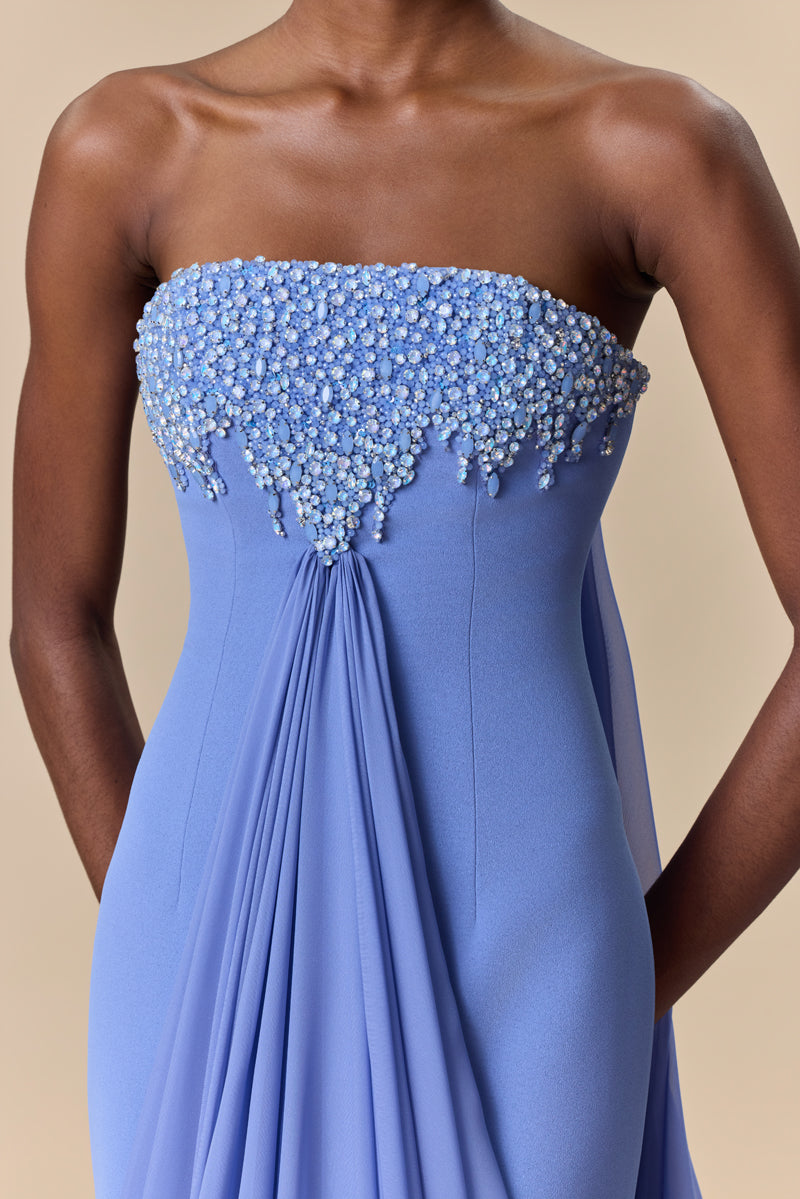 A strapless fitted crêpe dress featuring a straight neckline embellished with crystals with long, cascading chiffon drapes attached to the bodice.