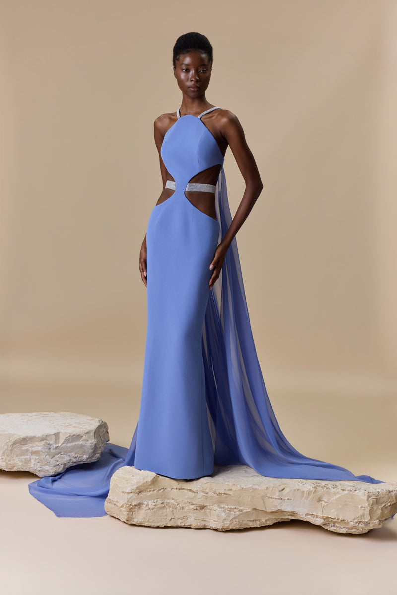A fitted crepe dress featuring a halter neckline, side waist cutouts with a beaded belt, and a flowing chiffon cape attached at the back.