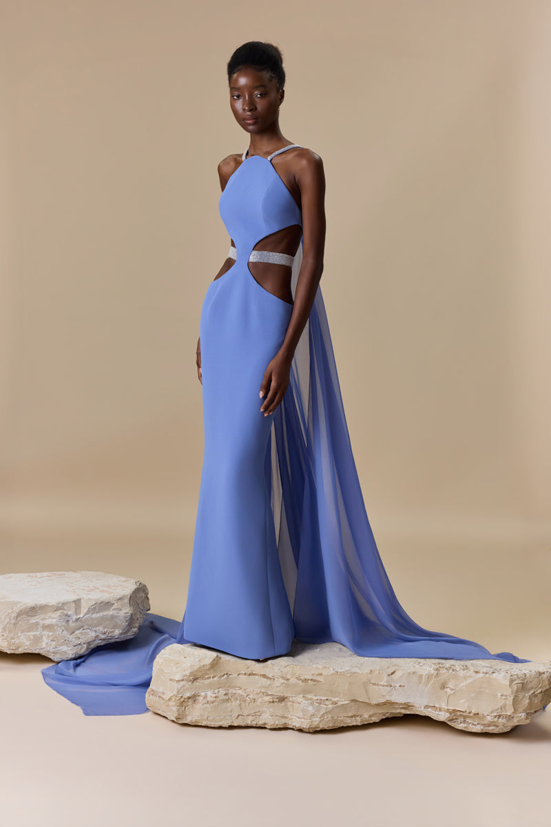 A fitted crepe dress featuring a halter neckline, side waist cutouts with a beaded belt, and a flowing chiffon cape attached at the back.