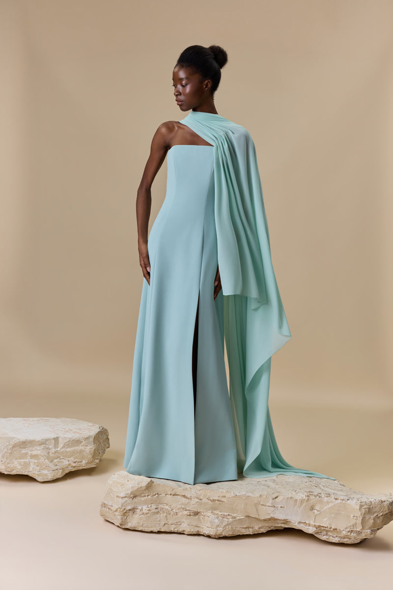 A strapless crepe dress featuring a high front slit and a sheer georgette asymmetric neckline layer that cascades into a sweeping side cape.