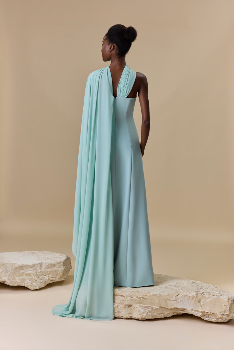 A strapless crepe dress featuring a high front slit and a sheer georgette asymmetric neckline layer that cascades into a sweeping side cape.