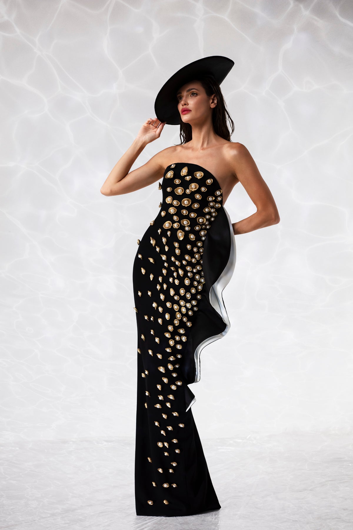 Corseted black crêpe column gown with an exploded ruffle, embroidered with pearls and gold hand-painted scallop shells