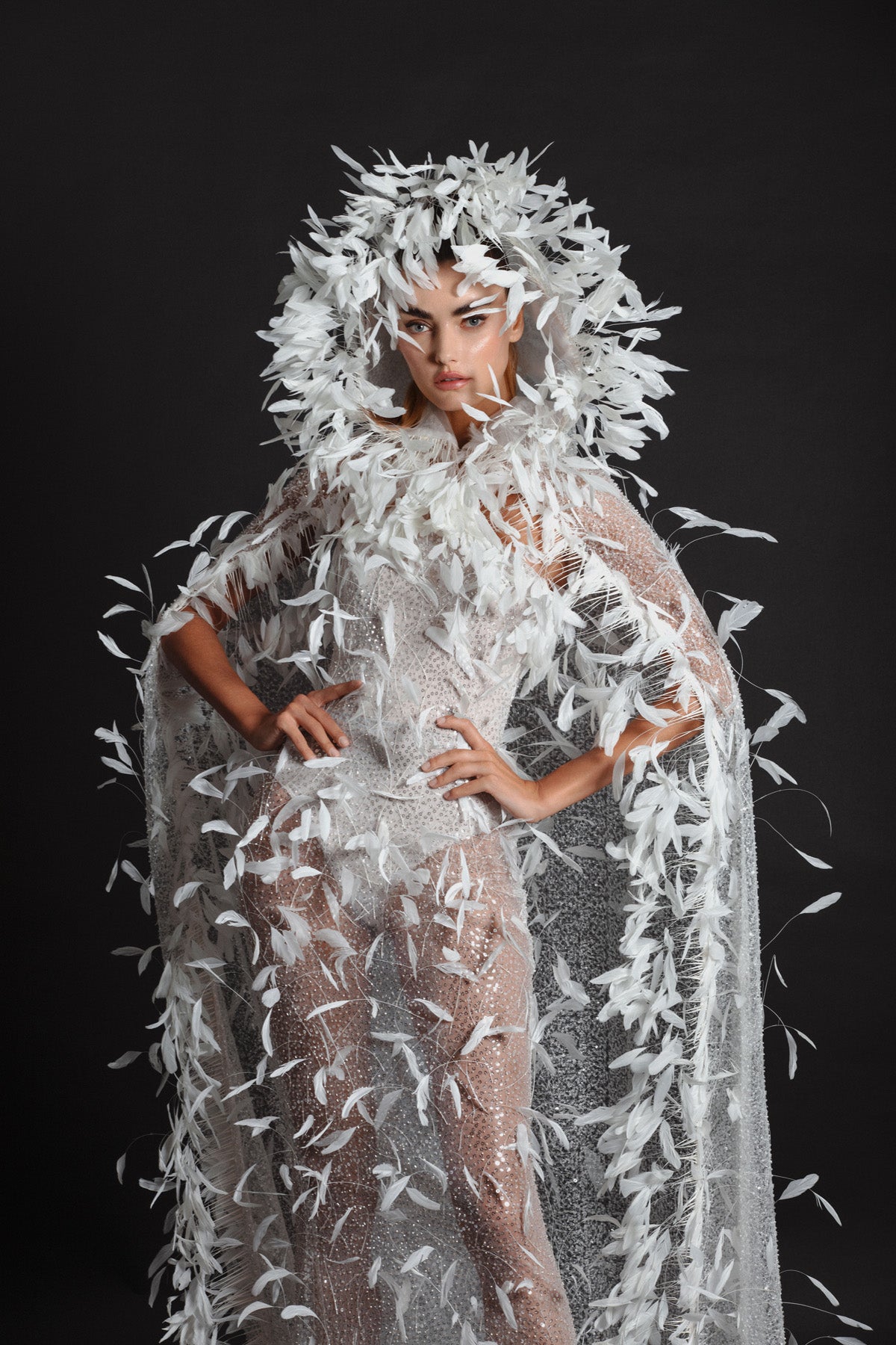 White tulle strapless gown worn with a hooded cape, hand appliquéd with coq plumes and embroidered with metallic silver threads, glass beads and sequins