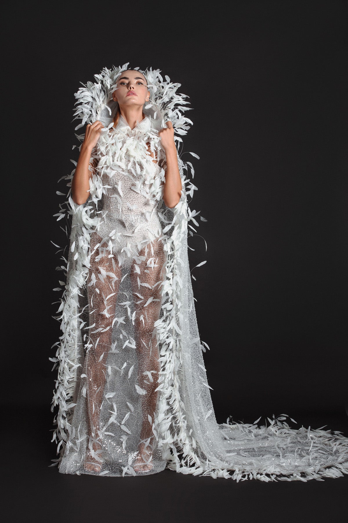 White tulle strapless gown worn with a hooded cape, hand appliquéd with coq plumes