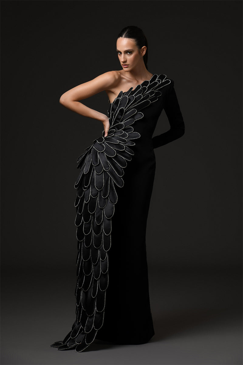 A sculpted gown in black crepe paired with a winged cape of layered hand-crafted plumes in scuba and crystals