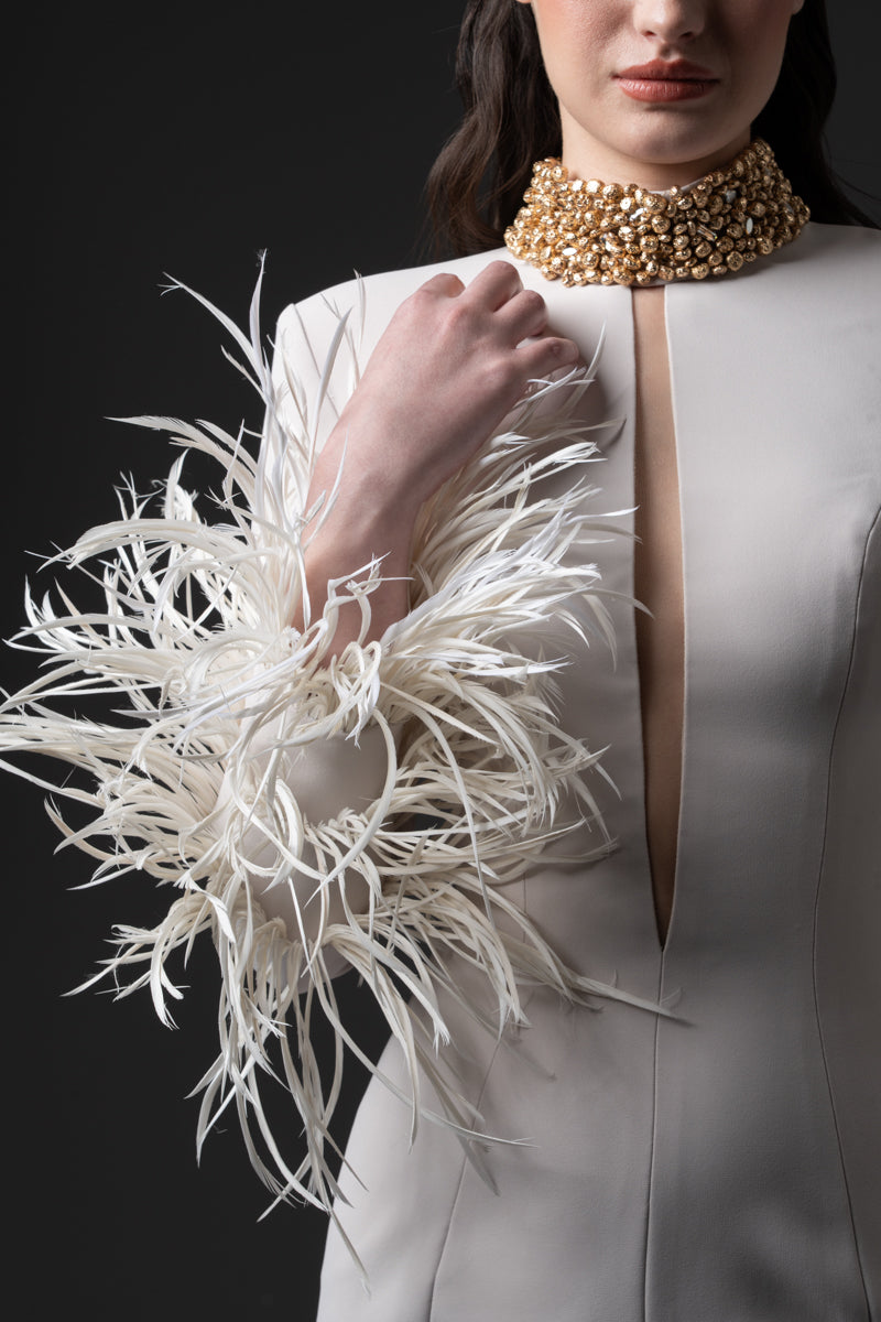 A fitted long sleeves dress with a beaded collar, a deep vertical opening  at the bust and feathers on the sleeves