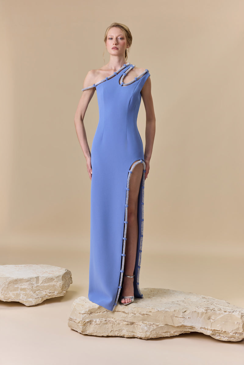A fitted crepe gown featuring an asymmetrical neckline and a high side slit, both finished with crystal-embellished cord.