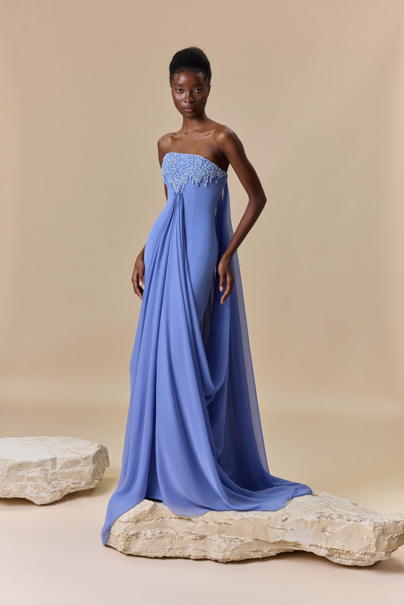 A strapless fitted crêpe dress featuring a straight neckline embellished with crystals with long, cascading chiffon drapes attached to the bodice.