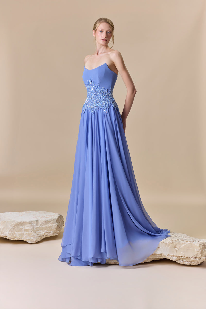 A strapless dress featuring a structured crepe bodice, a flowing chiffon skirt, and a crystal-beaded waist.