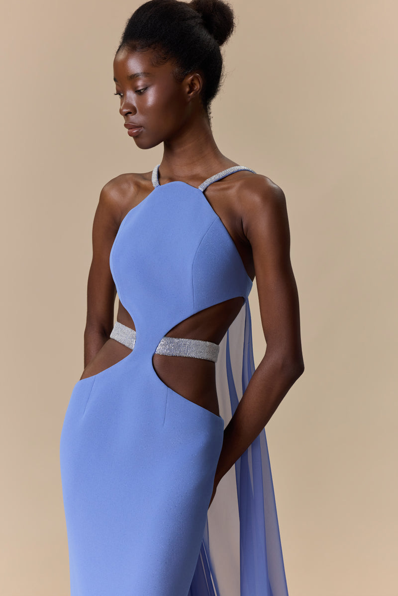 A fitted crepe dress featuring a halter neckline, side waist cutouts with a beaded belt, and a flowing chiffon cape attached at the back.