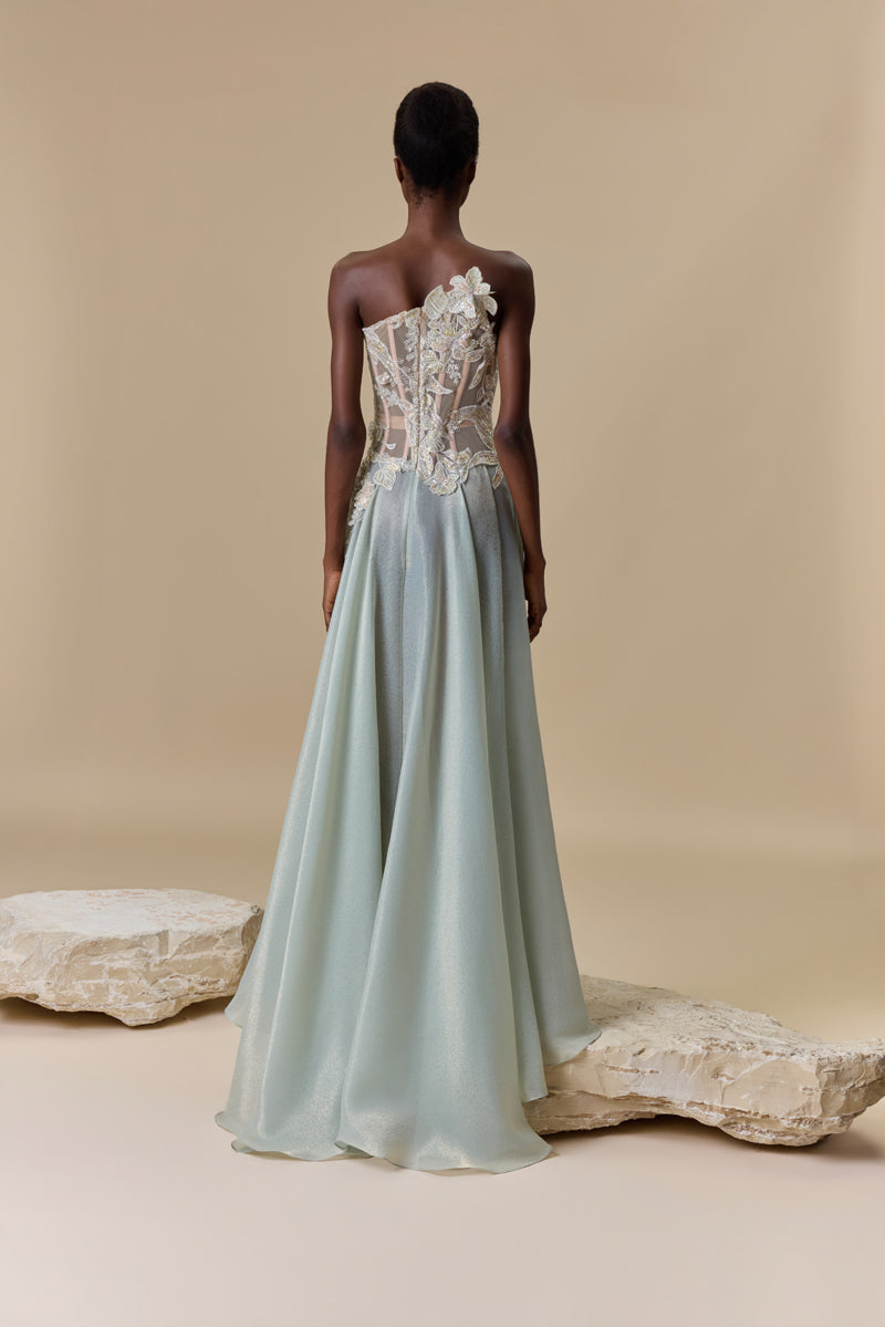 A strapless dress featuring an asymmetric bodice embellished with floral embroidery, paired with a flowing lame organza skirt.