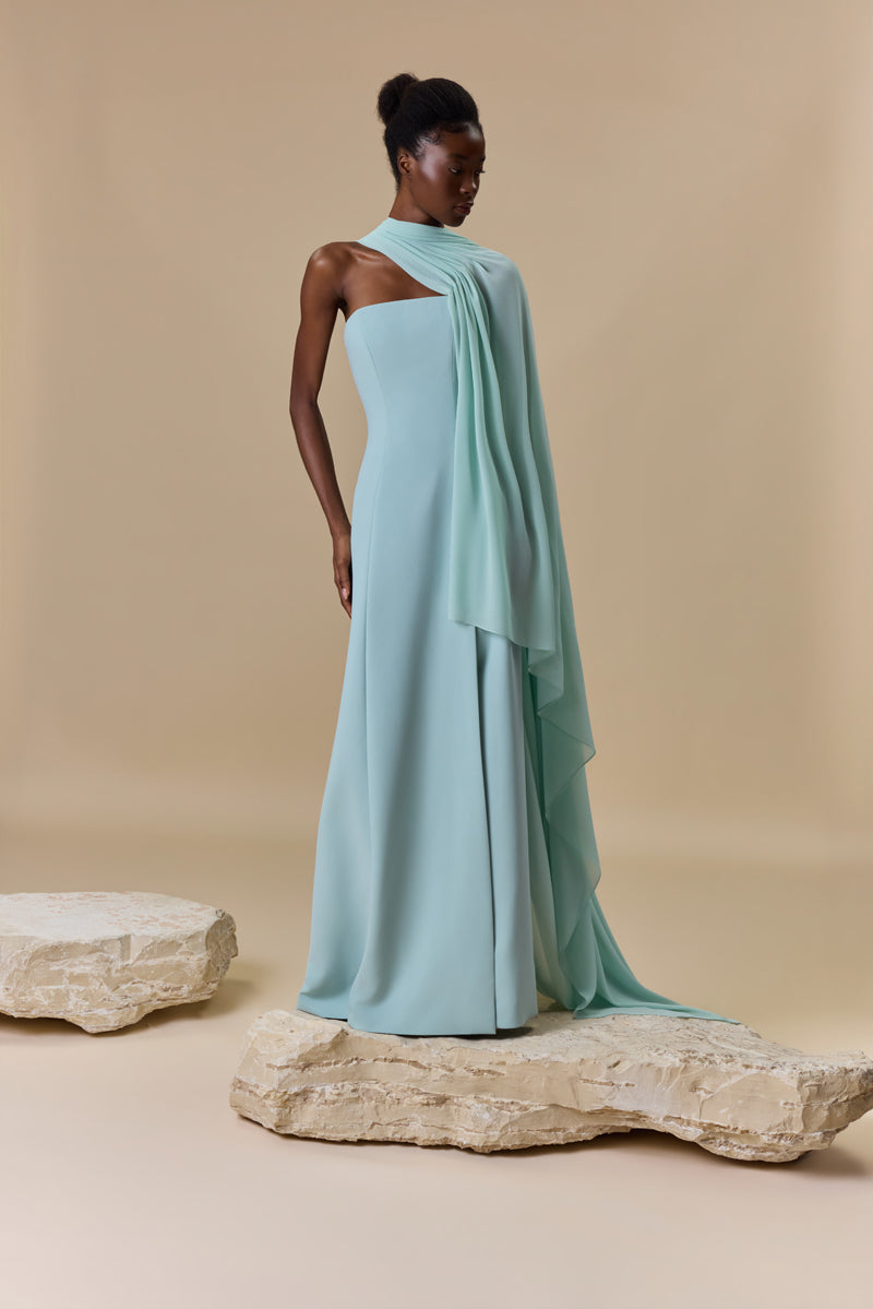 A strapless crepe dress featuring a high front slit and a sheer georgette asymmetric neckline layer that cascades into a sweeping side cape.