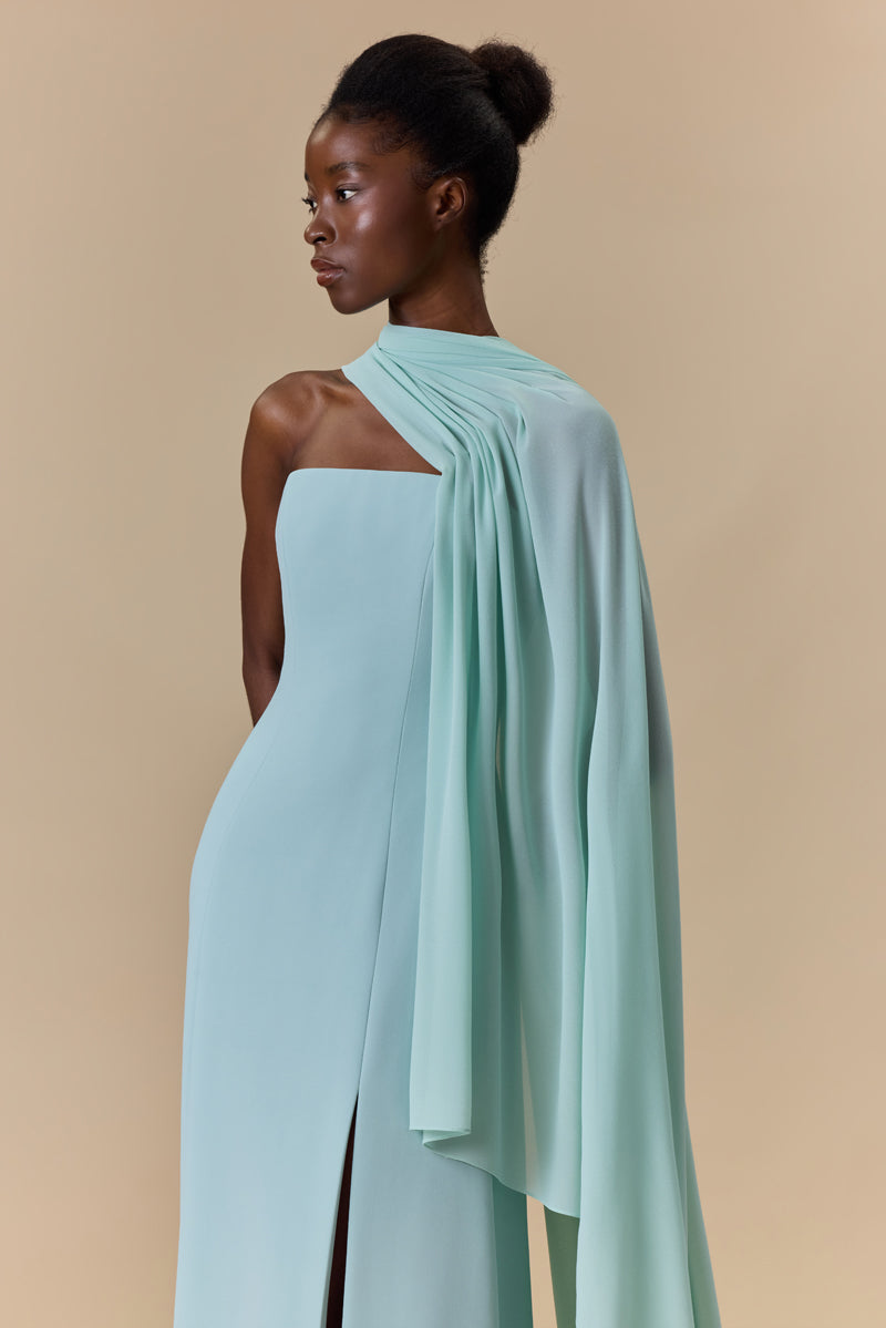 A strapless crepe dress featuring a high front slit and a sheer georgette asymmetric neckline layer that cascades into a sweeping side cape.