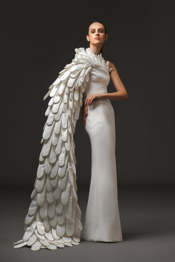 A sculpted gown in white silk scuba paired with layers of 3D hand-crafted plumes emerging from the bust into a cape