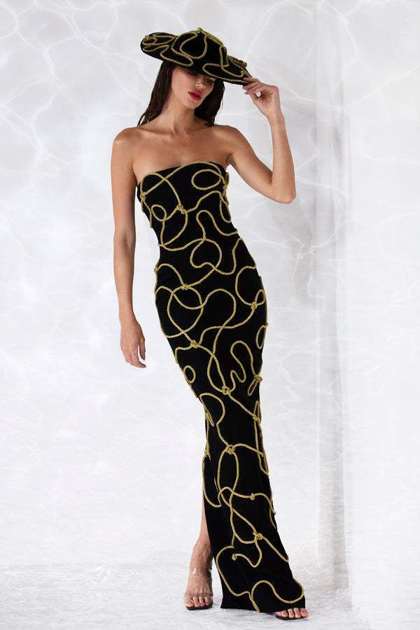 Strapless corseted black crêpe column gown embroidered with golden sailor knots. Worn with a black velvet matching hat.