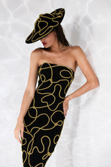 Corseted black crêpe column gown embroidered with golden sailor knots. Worn with a black velvet matching hat.
