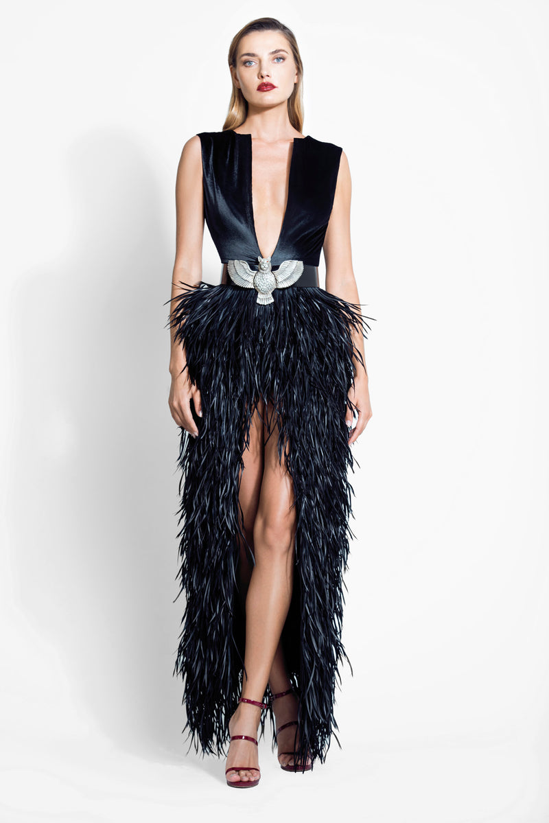 Plunging neckline gown crafted in black in black silk velvet embellished with layered twisted feathers and finished with a belt featuring a half-eagle half-lion mythical creature brooch