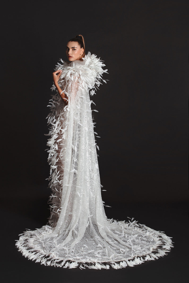 Sleeveless white tulle gown worn with a hooded cape, hand appliquéd with coq plumes and embroidered with metallic silver threads, glass beads and sequins