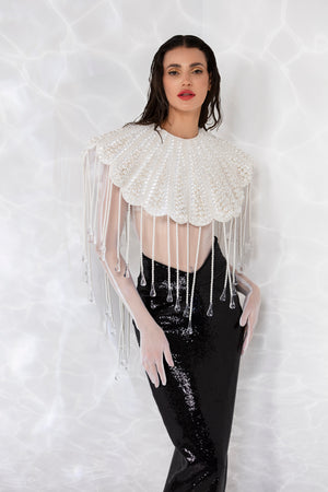 Round neck scallop shell inspired ensemble consisting of a cropped top embroidered with pearls, crystals, and hand blown glass drops. Worn with a white sheer bodysuit and a pencil skirt in high gloss sequins